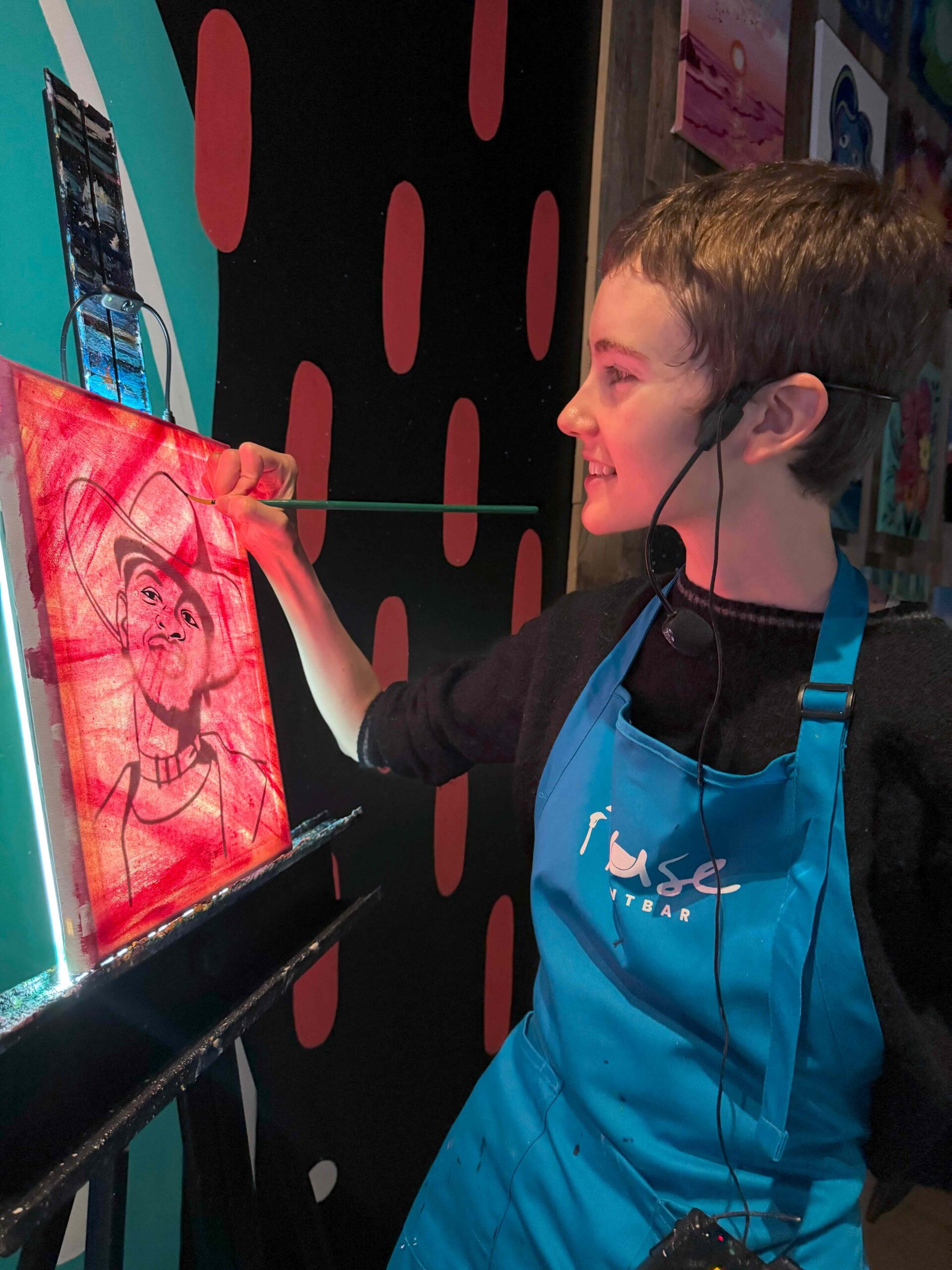 Instructor guiding a participant during a painting session at Muse Paintbar. Guests are enjoying a hands-on, creative experience in a vibrant studio filled with colorful artwork.